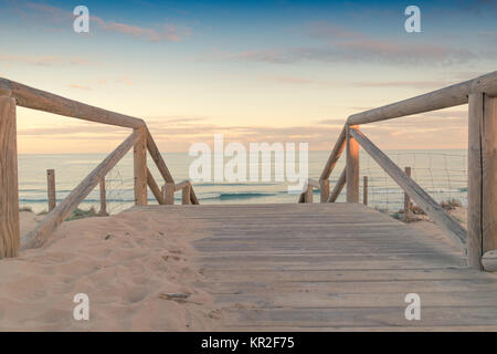 Hölzerne Treppe und Geländer Zugang zum Strand Sand bei Sonnenuntergang mit etwas bewölkter Himmel ein Meer mit Wellen in Guardamar in Spanien Stockfoto