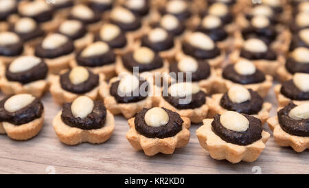 Detail der Coconut Cupcakes mit Schokoladenfüllung und Mandeln. Dekorative Süße Weihnachten Gebäck auf Holz Hintergrund gestapelt. Geringe Tiefe von sharpnes. Stockfoto