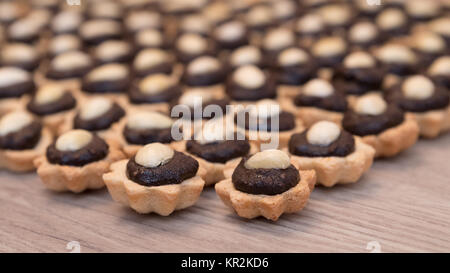 Coconut Cupcakes mit Schokoladenfüllung und Mandeln garnieren. Dekorative Süße Weihnachten Gebäck auf einem Holz Hintergrund gestapelt. Kleine Tiefe der Schärfe. Stockfoto
