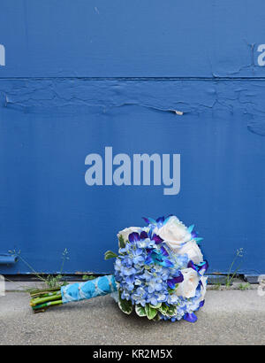 Foto von einem blauen und weißen Brautstrauß gegen ein Peeling Hintergrund. Blau bom dendrobium Orchideen und Hydrangea kombinieren schön mit weißen Rosen. Stockfoto