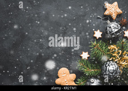 Stilvolle Weihnachten Hintergrund mit fallenden Schnee, vintage Weihnachten Spielzeug, Tannenbaum und Cookies auf schwarzen Stein Hintergrund. Ansicht von oben, kopieren Platz für Text. Stockfoto