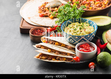 Hausgemachtes Rindfleisch mexikanische Fajitas mit Tortilla und Guacamole und Salsa Saucen auf schwarzem Hintergrund Stockfoto