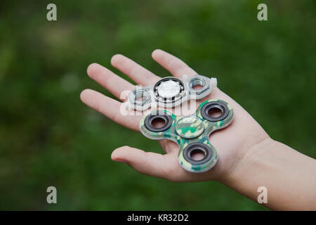 Kind Holding ungewöhnliche Metall handgefertigte Spinner und Grünen üblichen Spinner auf Palm an Verschwommene grüne Gras Hintergrund isoliert. Stockfoto