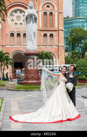 Hochzeit paar außerhalb der Kathedrale Notre Dame in Saigon posieren. Die vietnamesischen Bräute normalerweise in drei verschiedene Kleider während der Rezeption. Stockfoto