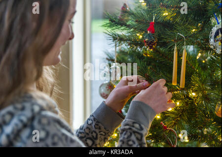 Nahaufnahme von Teenager schmücken einen Weihnachtsbaum mit leuchtenden Lampen. Stockfoto