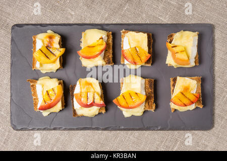 Kanapees, Vorspeise mit gegrilltem Brie und Nektarine auf einer Schiefertafel Schale vergoldet Stockfoto