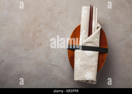 Geschlossene Holz- Japanische lunchbox mit Stäbchen, in einer festlichen Tuch auf einem alten steinernen Tisch gewickelt. Ansicht von oben mit der Kopie. Stockfoto