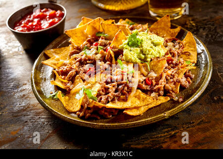 Gelber mais Nacho Chips garniert mit Hackfleisch, Guacamole, Käse, Paprika und Koriander Blätter in die Platte an der hölzernen Tisch Stockfoto