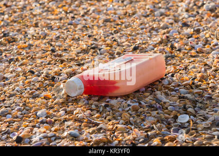 Kunststoff-Flaschen Motoröl am Strand ist übersät mit kleinen bunten Muscheln Stockfoto