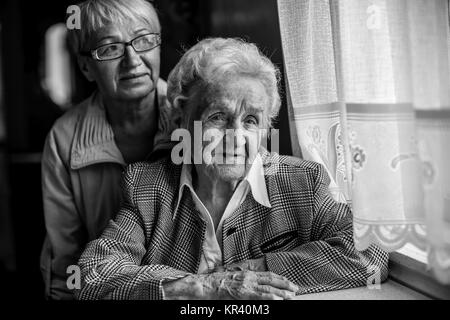 Eine ältere Frau am Tisch sitzen, neben einer erwachsenen Tochter. Schwarz-weiß Foto. Stockfoto