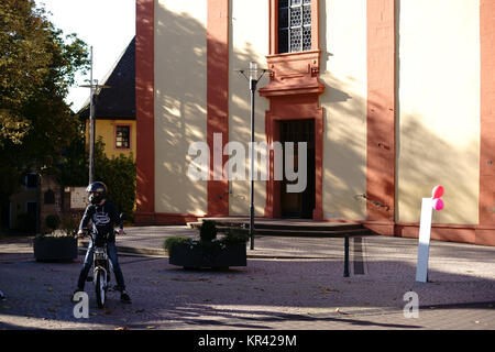 Nieder-Olm, Deutschland - 14. Oktober 2017: Mopedfahrer auf dem Vorplatz der Katholischen Pfarrkirche St. Georg am 14. Oktober 2017 in Nieder-Olm. Stockfoto