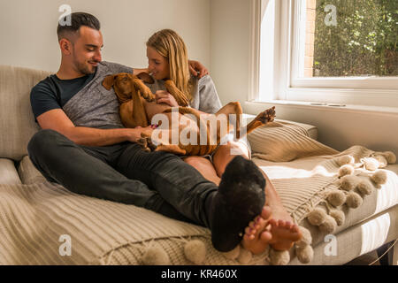 Paar auf Sofa kuscheln Hund Fenster Stockfoto