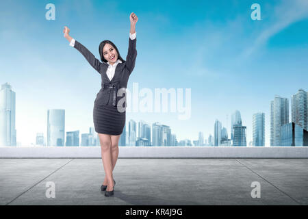 Aufgeregt Asian Business Frau, die auf der Dachterrasse mit blauem Himmel Hintergrund Stockfoto