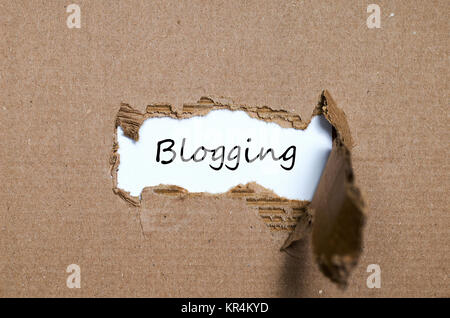 Das Wort Blogging erscheint hinter zerrissenes Papier Stockfoto