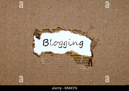 Das Wort Blogging erscheint hinter zerrissenes Papier Stockfoto