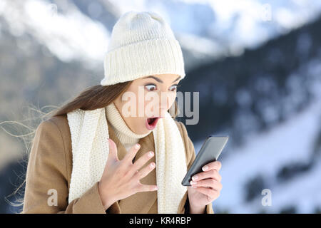 Erstaunt Frau liest online Nachrichten in einem Smart Phone im Winter Urlaub in die schneebedeckten Berge Stockfoto