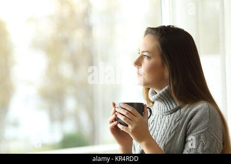 Seitenansicht Porträt einer nachdenklichen ernste Frau durch ein Fenster in ein trauriger Tag suchen Stockfoto