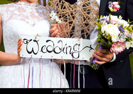 Hochzeit-Dekor. Hölzerne Gedenktafel mit der Inschrift Hochzeit. Hochzeit auf einem Teller grüner Hintergrund und ein Brunnen. Hochzeitsdekorationen. Stockfoto