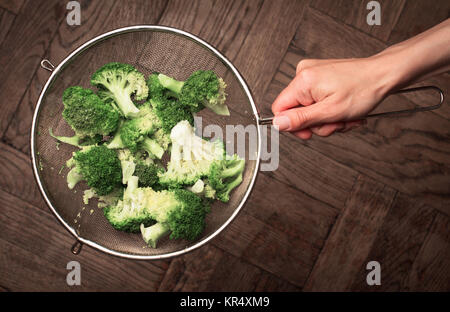 Blick von oben auf die eine Hand mit einem Sieb mit Schneiden Brokkoli Stockfoto