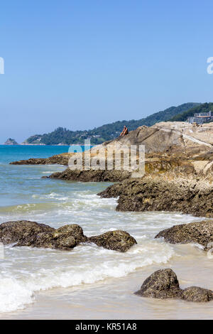 Man saß auf Felsen am nördlichen Ende des Patong Strand, Phuket, Thailand Stockfoto