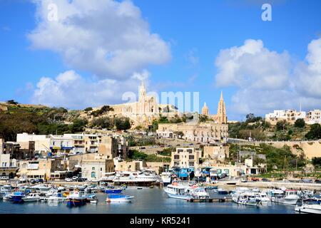 Blick auf die Boote im Hafen mit der ghajnsielem Pfarrkirche und Unserer Lieben Frau von Lourdes Kirche auf der Rückseite, Mgarr, Gozo, Malta, Europa. Stockfoto