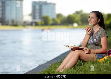 Schwangere Frau mit Buch sitzt im Park. Stockfoto
