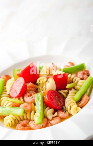 Pasta mit Gemüse und Garnelen auf dem weißen Hintergrund vertikal Stockfoto