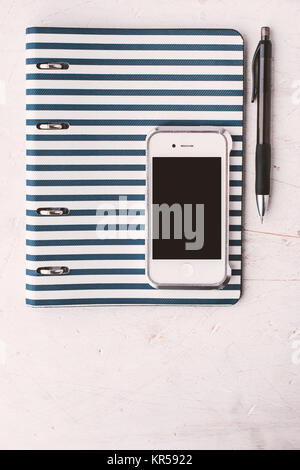 Notebook mit Stift und Telefon am weißen Tisch vertikal Stockfoto