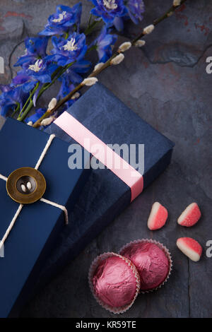 Frühling Geschenk mit Süßigkeiten und Blumen auf einem blauen Stein Hintergrund Stockfoto