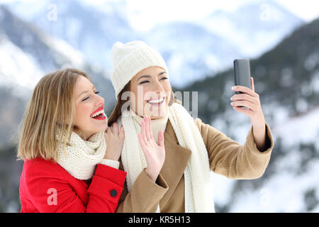 Zwei glückliche Touristen in einer Videokonferenz mit einem Smart Phone im Winter Urlaub in die schneebedeckten Berge Stockfoto