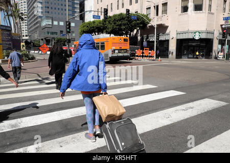 Rückansicht einer Frau mit Gepäck und Taschen, die auf einem Quersteg auf der W 5th Street und Hill Street in der Innenstadt von Los Angeles, Kalifornien, USA, läuft KATHY DEWITT Stockfoto