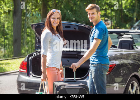 Lächelndes Paar Gepäck im Kofferraum eines Autos Stockfoto