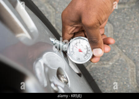 Person mit Manometer für die Messung des Reifendrucks Stockfoto