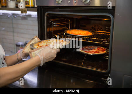 7/8 Schuß von den Händen der Köchin in der Küche die Pizza aus dem Ofen Handschuh. Readiness Test Stockfoto