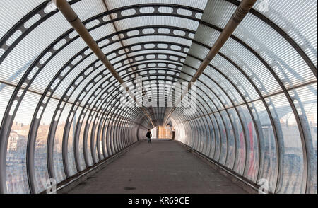 London, England, UK - 10. Dezember 2011: Ein Fußgänger Spaziergänge entlang eine moderne, verglaste Fußgängerbrücke in der Nähe der Docklands East London. Stockfoto