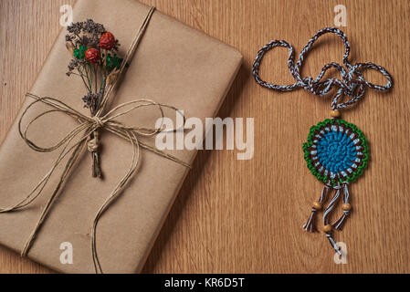 Buch ist in braunem Papier gewickelt, gebunden mit Papier thread liegen auf der Tischplatte mit einem gestrickten Medaillon daneben liegen. Stockfoto