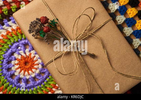 Wickelte Buch mit braunem Papier thread mit kleinen getrockneten Blumenstrauß aus Feld Pflanzen gebunden auf dem Tisch liegt auf zwei bunte gestrickte Servietten. Stockfoto