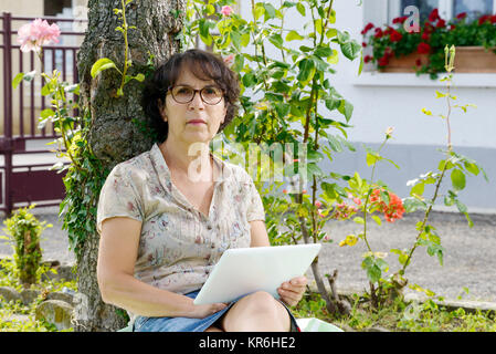 Reife Frau sitzend mit einem Tablett in den Garten Stockfoto