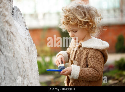 Wenig adorable blonde Mädchen, die den Baum mit weißer Farbe gegen Nagetiere im Garten im Frühling zu schützen. Stockfoto