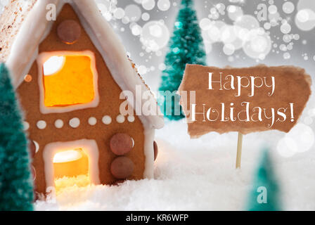 Lebkuchenhaus in der verschneiten Landschaft als Weihnachtsdekoration. Weihnachtsbäume und Kerzen für romantische Atmosphäre. Silberner Hintergrund mit Bokeh Wirkung. Englischer Text frohe Feiertage Stockfoto