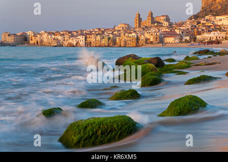 Blick entlang der Küste mit Sandstrand, Felsen, mit grünen Algen, die Stadt in der Ferne. Stockfoto