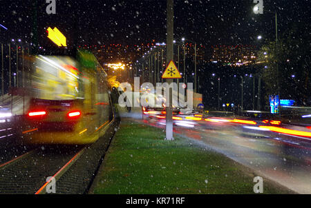 Erster Schnee in der Stadt bei Nacht. Verschwommen lichter Autos und Straßenbahn auf Stadt Straße mit Schneeflocken im ersten Plan. Stockfoto