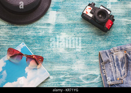 Reise Zubehör auf einem blauen Hintergrund Holz - ein Film Kamera, denim Shorts, ein schwarzes Stroh Hut, ein Notebook und rosa Sonnenbrille. Platz für einen Text o Stockfoto