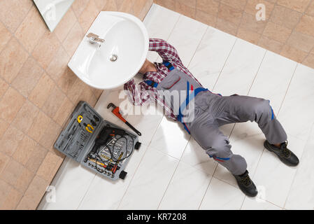 Männliche Klempner liegend auf dem Boden Instandsetzung Waschbecken im Badezimmer Stockfoto