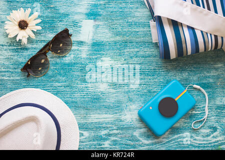 Traveler Essentials auf Blau Holz- Hintergrund - schwarze Sonnenbrille, eine Kamera, einen Strand und einen weißen Hut. Platz für einen Text oder ein Produkt anzeigen, Ansicht von oben. Stockfoto