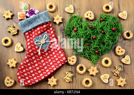 Weihnachten Socke mit Geschenken und Bäckerei Hintergrund mit Cookies und Herzen von Tannenzweigen mit roten Früchten. Stockfoto