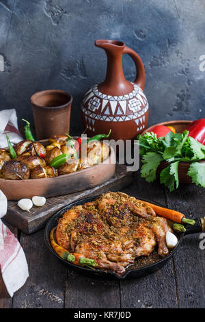 Ganze Hähnchen in eine eiserne Pfanne mit gebackenen Kartoffeln und Wein. Georgische tapaka Huhn. Dunkler Hintergrund Stockfoto