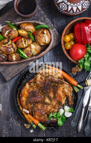 Ganze Hähnchen in eine eiserne Pfanne auf dunklem Hintergrund, Ansicht von oben. Stockfoto