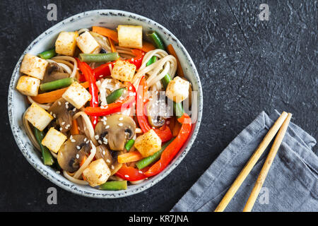 Pfannengerichte mit Udon-nudeln, Tofu, Pilzen und Gemüse. Asiatische vegan vegetarisch essen, Mahlzeit, Bundesrepublik Jugoslawien über schwarzen Hintergrund rühren, kopieren. Stockfoto