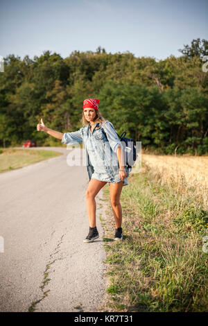 Junge Frau per Anhalter Fahren auf einer Landstraße Stockfoto
